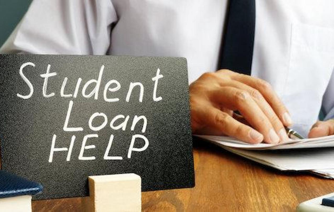 A sign reading "Student Loan Help" in front of a person looking at paperwork.
